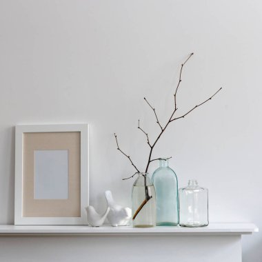 İskandinav tarzı. Dallı bir şişe su, farklı şekillerde iki boş şişe, beyaz bir şöminenin üzerinde kuş heykelcikleri. Boşluğu kopyala
