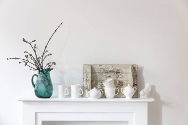 Yeşil cam bir kavanozda Amerikan akçaağaç dalları, porselen bardaklar, biblolar, beyaz bir çekmecede çaydanlık. İskandinav tarzı