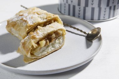 Elma Charlotte, porselen bir tabakta süzme peynir kremi ve masada bir fincan çay..