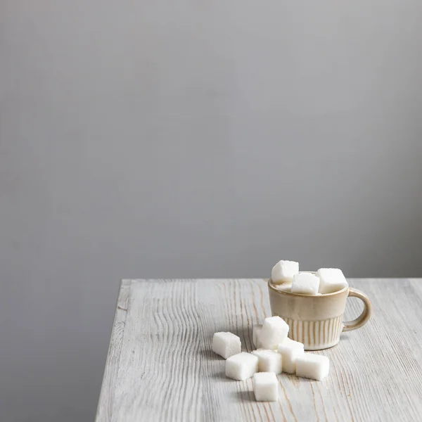 Cup with refined sugar in pieces scattered on the table