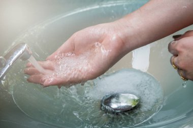 Lavaboda akan musluk suyunun altında ellerini yıkamak.