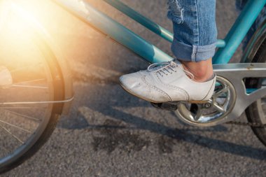 Kot giyen ve beyaz ayakkabı giyen bir kadın parkta bisiklet sürüyor.