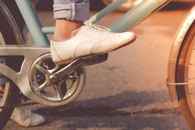 Kot giyen ve beyaz ayakkabı giyen bir kadın parkta bisiklet sürüyor.