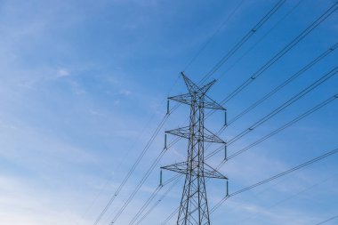 Gün batımından önce mavi gökyüzü olan yüksek voltajlı posta kulesi.