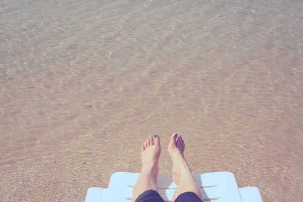 熱帯ビーチでの休暇澄んだ海の水の背景を持つビーチベッドの上の女性の足 — ストック写真