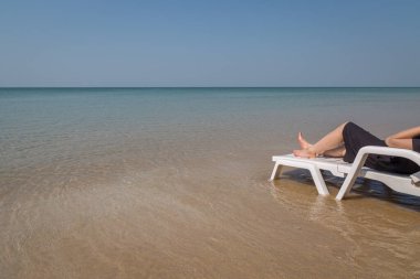 Tropikal plajda tatil. Plaj yatağında kadın bacakları. Temiz okyanus suyu arka planında.