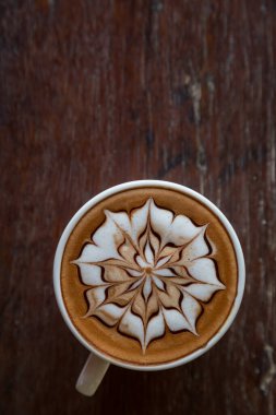 Üzerinde latte resmi olan bir fincan kahve ve ahşap masa arkası.