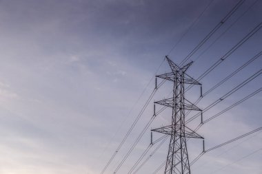 Gün batımından önce mavi gökyüzü olan yüksek voltajlı posta kulesi.