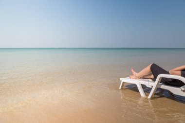 Tropikal plajda tatil. Plaj yatağında kadın bacakları. Temiz okyanus suyu arka planında.