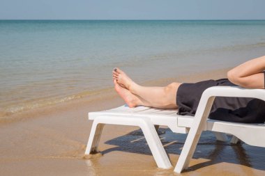 Tropikal plajda tatil. Plaj yatağında kadın bacakları. Temiz okyanus suyu arka planında.