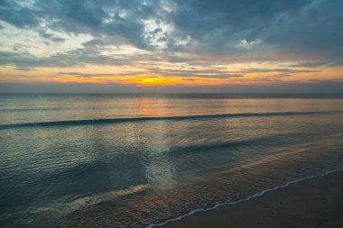 Güneş doğarken kumlu sahilde yumuşak bir mavi okyanus dalgası.