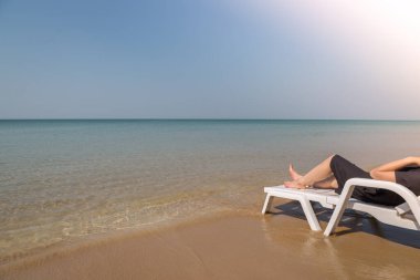 Tropikal plajda tatil. Plaj yatağında kadın bacakları. Temiz okyanus suyu arka planında.