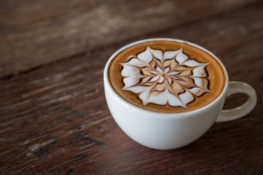 Üzerinde latte resmi olan bir fincan kahve ve ahşap masa arkası.