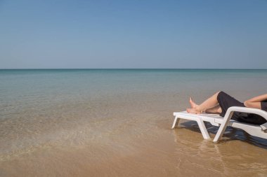 Tropikal plajda tatil. Plaj yatağında kadın bacakları. Temiz okyanus suyu arka planında.