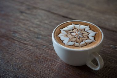 Üzerinde latte resmi olan bir fincan kahve ve ahşap masa arkası.
