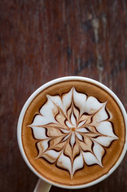 Üzerinde latte resmi olan bir fincan kahve ve ahşap masa arkası.