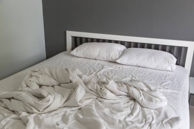 Yatakta iki beyaz yastık, yatak odasında kırışık, dağınık bir battaniye.