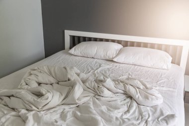 Yatakta iki beyaz yastık, yatak odasında kırışık, dağınık bir battaniye.