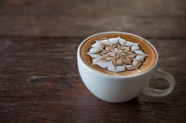Üzerinde latte resmi olan bir fincan kahve ve ahşap masa arkası.