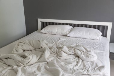 Yatakta iki beyaz yastık, yatak odasında kırışık, dağınık bir battaniye.