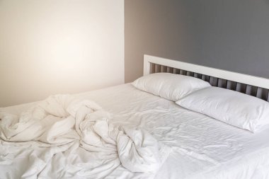 Yatakta iki beyaz yastık, yatak odasında kırışık, dağınık bir battaniye.