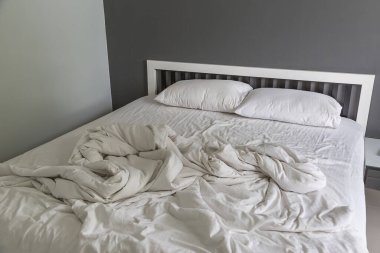 Yatakta iki beyaz yastık, yatak odasında kırışık, dağınık bir battaniye.