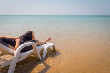 Tropikal plajda tatil. Plaj yatağında kadın bacakları. Temiz okyanus suyu arka planında.