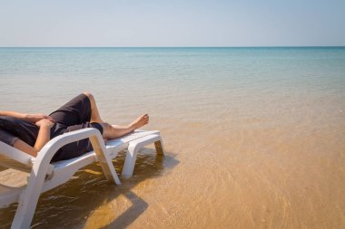 Tropikal plajda tatil. Plaj yatağında kadın bacakları. Temiz okyanus suyu arka planında.