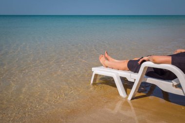Tropikal plajda tatil. Plaj yatağında kadın bacakları. Temiz okyanus suyu arka planında.