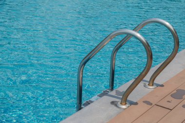 Merdiven merdiveni ve mavi su arka planlı yüzme havuzu.