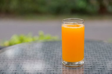 Masa camında yeşil arka planlı portakal suyu bardağı var.