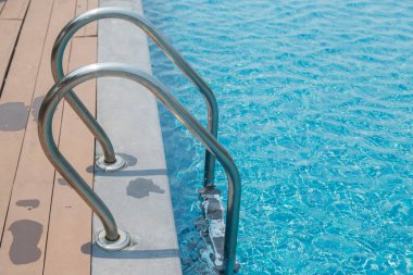 Merdiven merdiveni ve mavi su arka planlı yüzme havuzu.