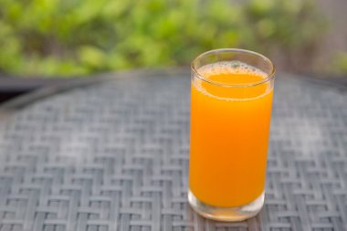 Masa camında yeşil arka planlı portakal suyu bardağı var.