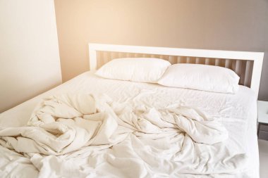 Yatak odasında kırışıklıkları olan iki beyaz yastık ve battaniye.