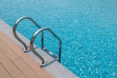 Merdiven merdiveni ve mavi su arka planlı yüzme havuzu.