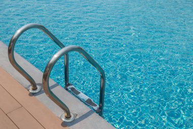 Merdiven merdiveni ve mavi su arka planlı yüzme havuzu.