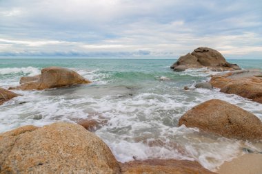 Kumsalda kum ve mavi gökyüzü zeminli deniz ve kaya taşları