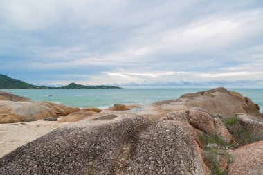 Kumsalda kum ve mavi gökyüzü zeminli deniz ve kaya taşları