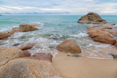 Kumsalda kum ve mavi gökyüzü zeminli deniz ve kaya taşları