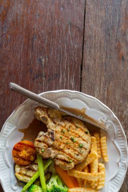 Ahşap masa arkasında beyaz tabakta siyah biberli domuz pirzolası.