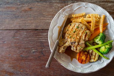 Ahşap masa arkasında beyaz tabakta siyah biberli domuz pirzolası.