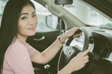 Asyalı kız gülümsüyor rahatlıyor oturuyor ve yeni arabada sürüş güvenliğini sağlıyor.