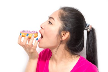 Güzel, uzun siyah saçlı, beyaz arka planda pembe çörek yiyen bir kadın.