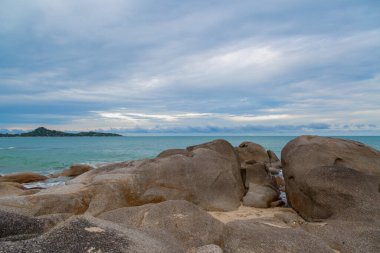 Kumsalda kum ve mavi gökyüzü zeminli deniz ve kaya taşları