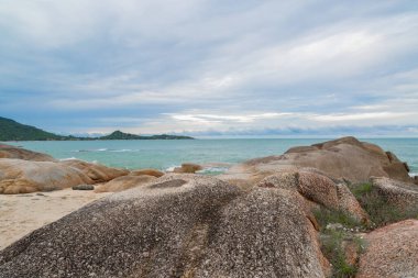 Kumsalda kum ve mavi gökyüzü zeminli deniz ve kaya taşları