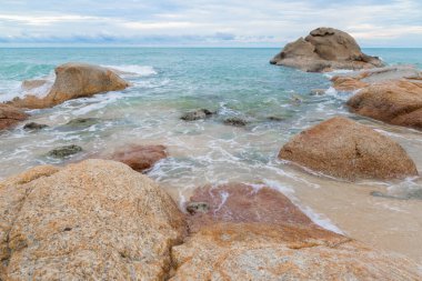 Kumsalda kum ve mavi gökyüzü zeminli deniz ve kaya taşları
