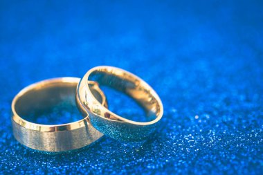 Gelin ve damadın altın alyansları koyu mavi renkli arka planda.