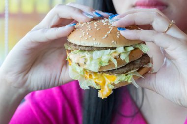 Mutlu genç bir kadın, mutlu bir şekilde hamburger yiyor.