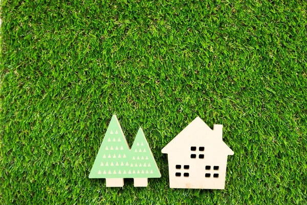 Yapay çimlerin üzerinde ağaç olan küçük ahşap bir ev.