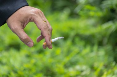 Yeşil doğal arka planda sigara tutan bir adamın eli.